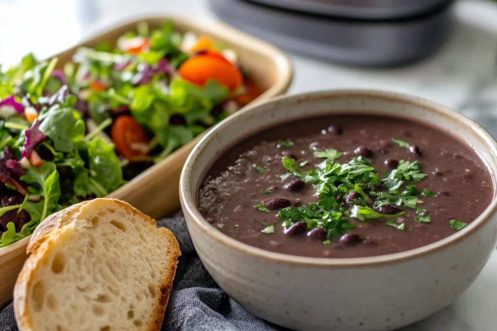 Purple black bean soup served with salad and bread, with leftovers stored in a container in the background.